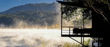 Una cabaña junto al lago con vistas a montañas envueltas en niebla.