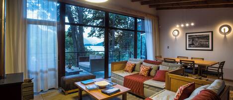 A cozy living room with a large window overlooking a scenic view, wooden furniture, and a dining area.