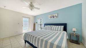 A bedroom with a bed, a ceiling fan, a window, and a door.