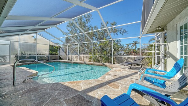 A covered outdoor swimming pool with clear blue water, surrounded by stone tiles and equipped with a metal ladder.
