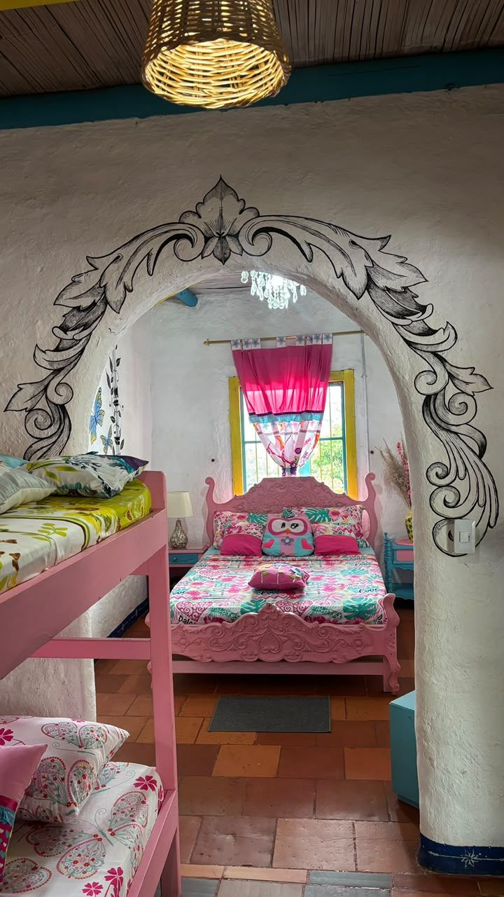 Un dormitorio con cama rosa, un arco decorativo y una ventana con cortinas.