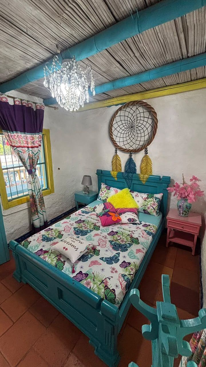 A bedroom with a bed, a nightstand, a lamp, a dreamcatcher, and a window with curtains.