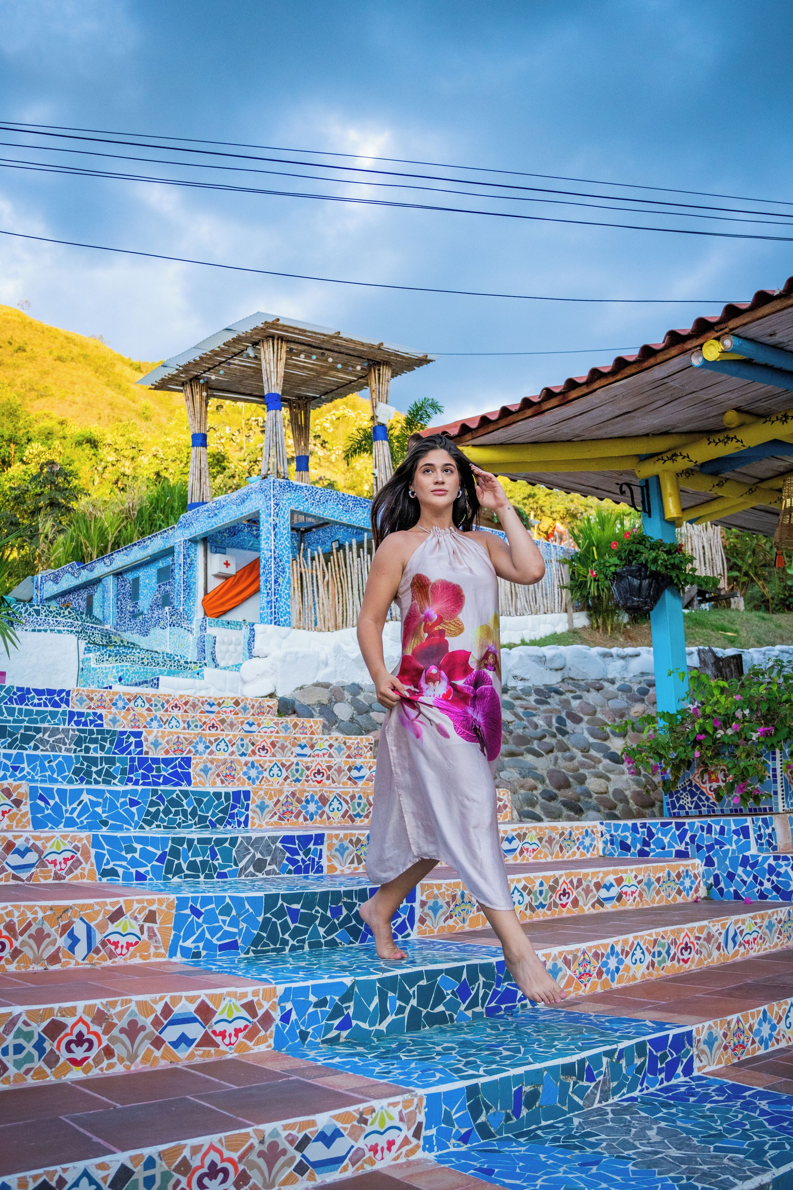 Una mujer parada sobre escalones de mosaico colorido, con un pabellón al fondo.