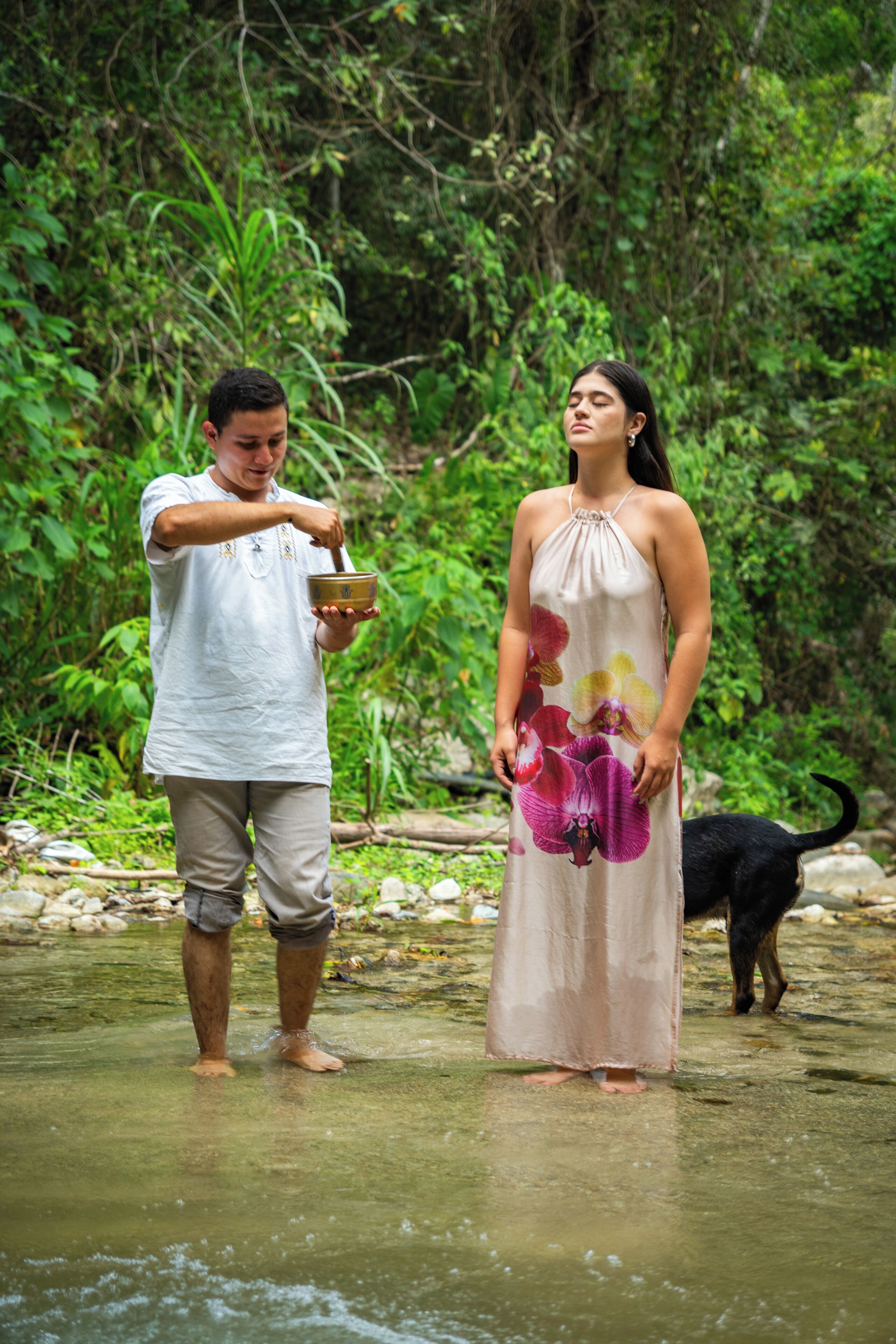 A man and a woman standing in a shallow stream, surrounded by lush greenery.