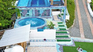 A large outdoor swimming pool with a tiled deck, surrounded by a lush green landscape and a white fence. - Bio Habitat Entre Montañas (Gigante)
