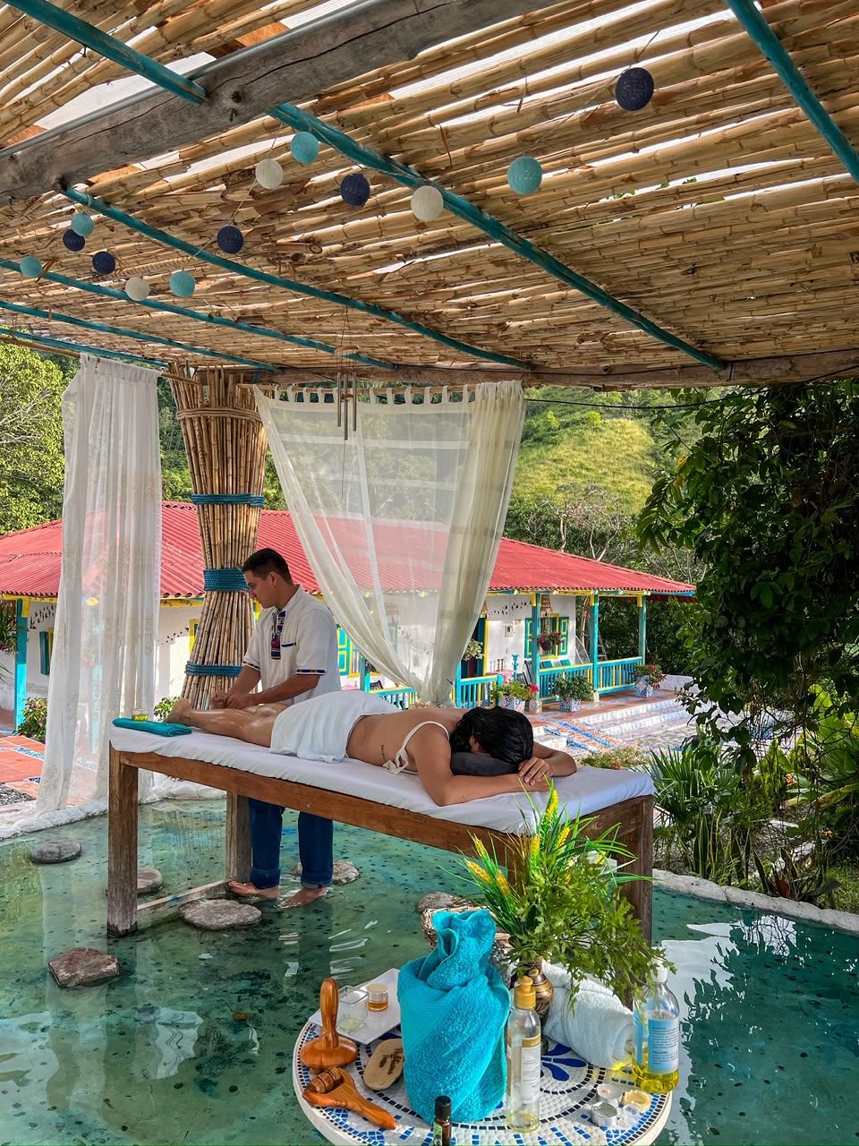 Sesión de masajes en un espacio exterior cubierto con piscina, camilla y diversos servicios.