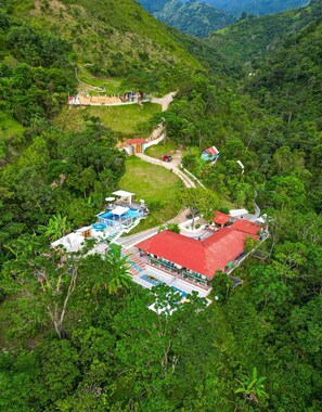 A resort with multiple buildings, a swimming pool, and a red-roofed structure surrounded by lush greenery. - Bio Habitat Entre Montañas (Gigante)