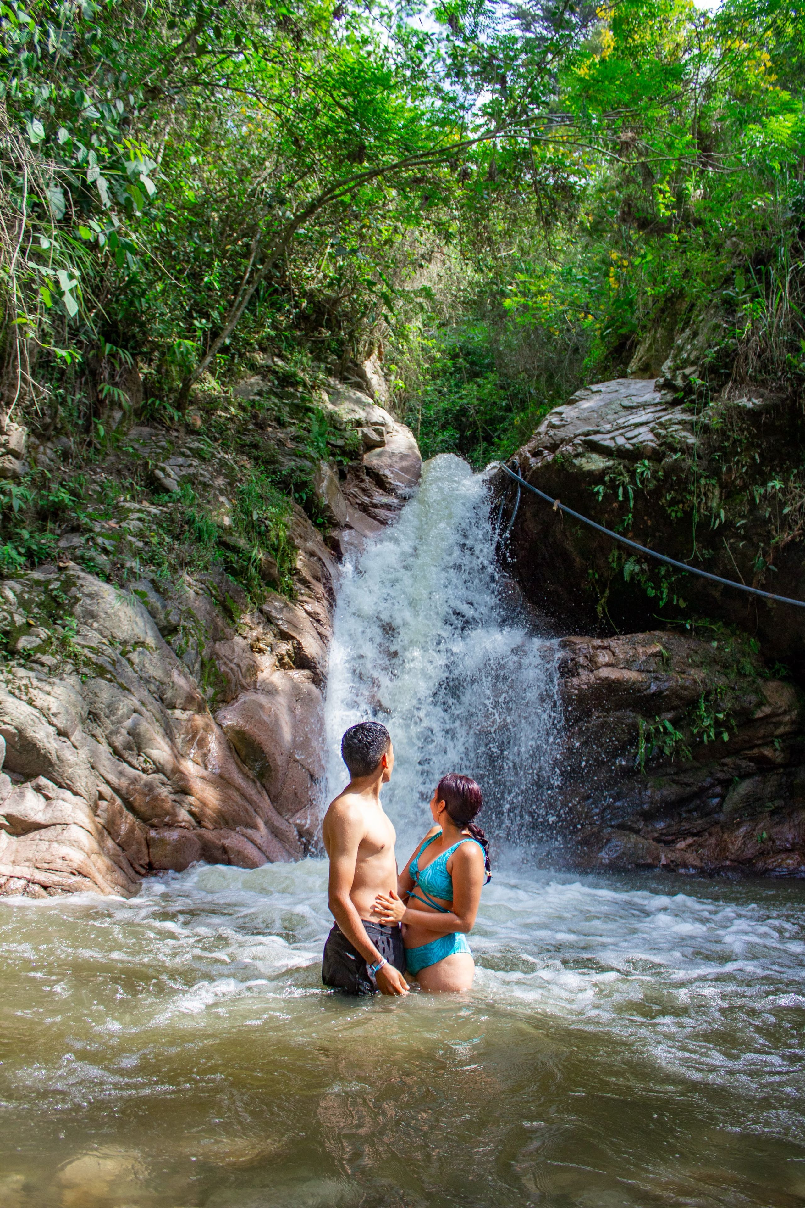 A natural water feature with a waterfall, surrounded by greenery.