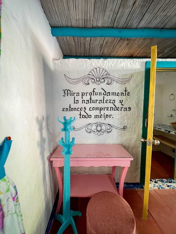 Una habitación pequeña con una mesa rosa y una silla, una pared decorativa con un mensaje y un techo de madera.