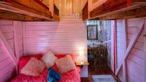 A cozy attic bedroom with a sloped ceiling, wooden beams, a bed with pink bedding, and a small bedside table with a lamp. - Bio Habitat Entre Montañas (Gigante)