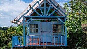 A small, elevated wooden house with a sloped roof, a porch with chairs, and a white door. - Bio Habitat Entre Montañas (Gigante)