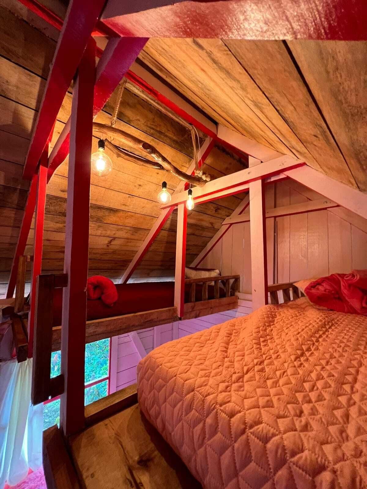 Un dormitorio acogedor en el ático con techo de madera, colcha acolchada y almohada roja.