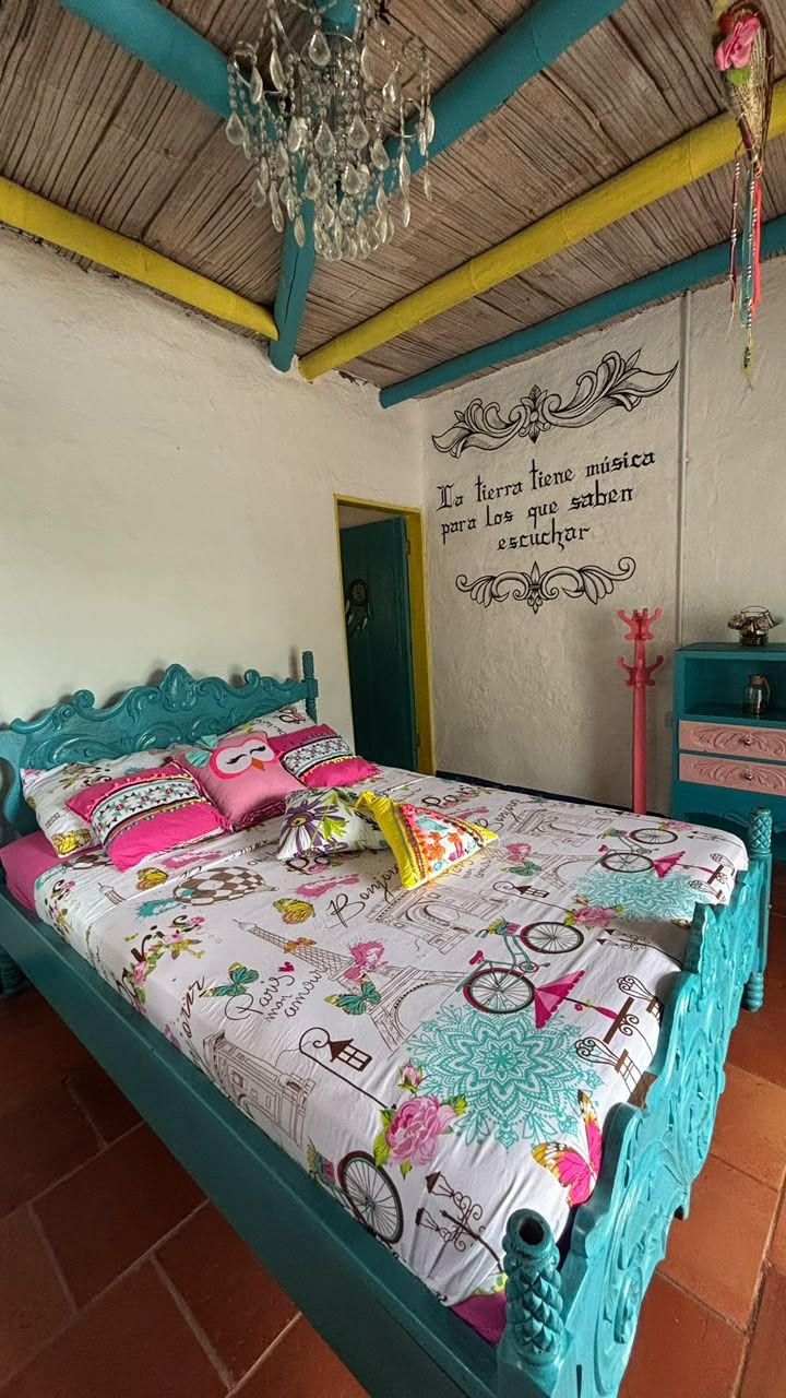 Una cama con colcha estampada, cabecera color turquesa y pared decorativa con una cita.