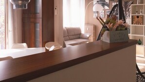 A modern living room with a wooden coffee table, a sofa, and a dining area with a table and chairs. There are two pendant lights hanging from the ceiling. - FORUM-Matteotti 12  (Assago)