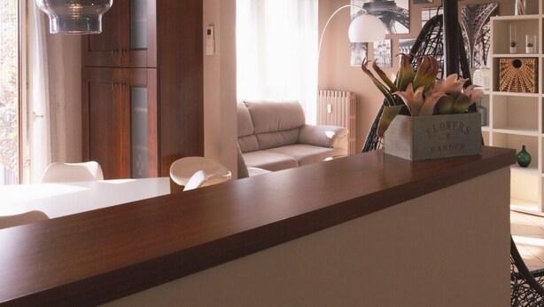 A modern living room with a wooden coffee table, a sofa, and a dining area with a table and chairs. There are two pendant lights hanging from the ceiling. - FORUM-Matteotti 12  (Assago)