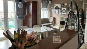 A modern living room with a dining area, featuring pendant lights, a sofa, a coffee table, and a hanging chair. - FORUM-Matteotti 12  (Assago)