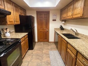 A kitchen with wooden cabinets, a black refrigerator, granite countertops, and a tiled floor. - Snowed Inn Brian Head Condo Sleeps 6 (Brian Head)