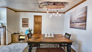 A dining area with a wooden table, chairs, a chandelier, a painting, and a wooden cabinet. - Snowed Inn Brian Head Condo Sleeps 6 (Brian Head)