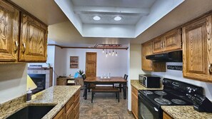 A kitchen with wooden cabinets, granite countertops, a dining table, and a stove. - Snowed Inn Brian Head Condo Sleeps 6 (Brian Head)