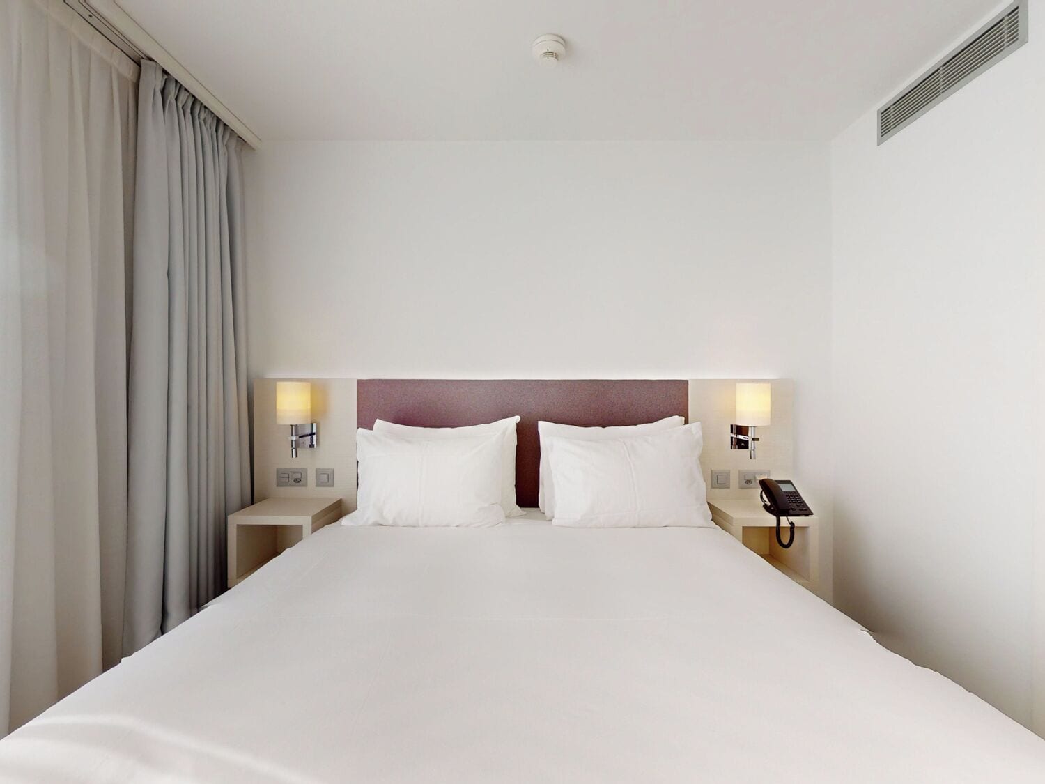 Une chambre d’hôtel avec un grand lit, deux tables de chevet avec des lampes, un téléphone et un luminaire fixé au mur.