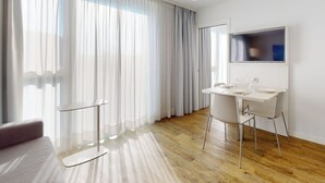 A modern hotel room with a wooden floor, a glass table with chairs, a sofa, and a TV mounted on the wall. - Nonanteneuf Vevey (Vevey)