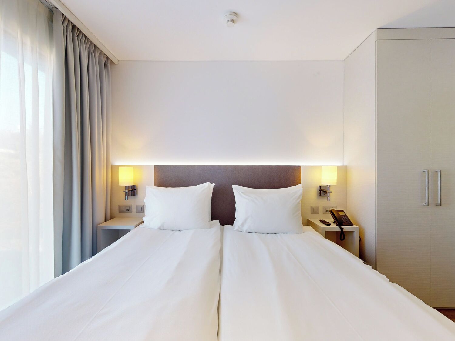 A hotel room with a large bed, two bedside tables, a wardrobe, and curtains.