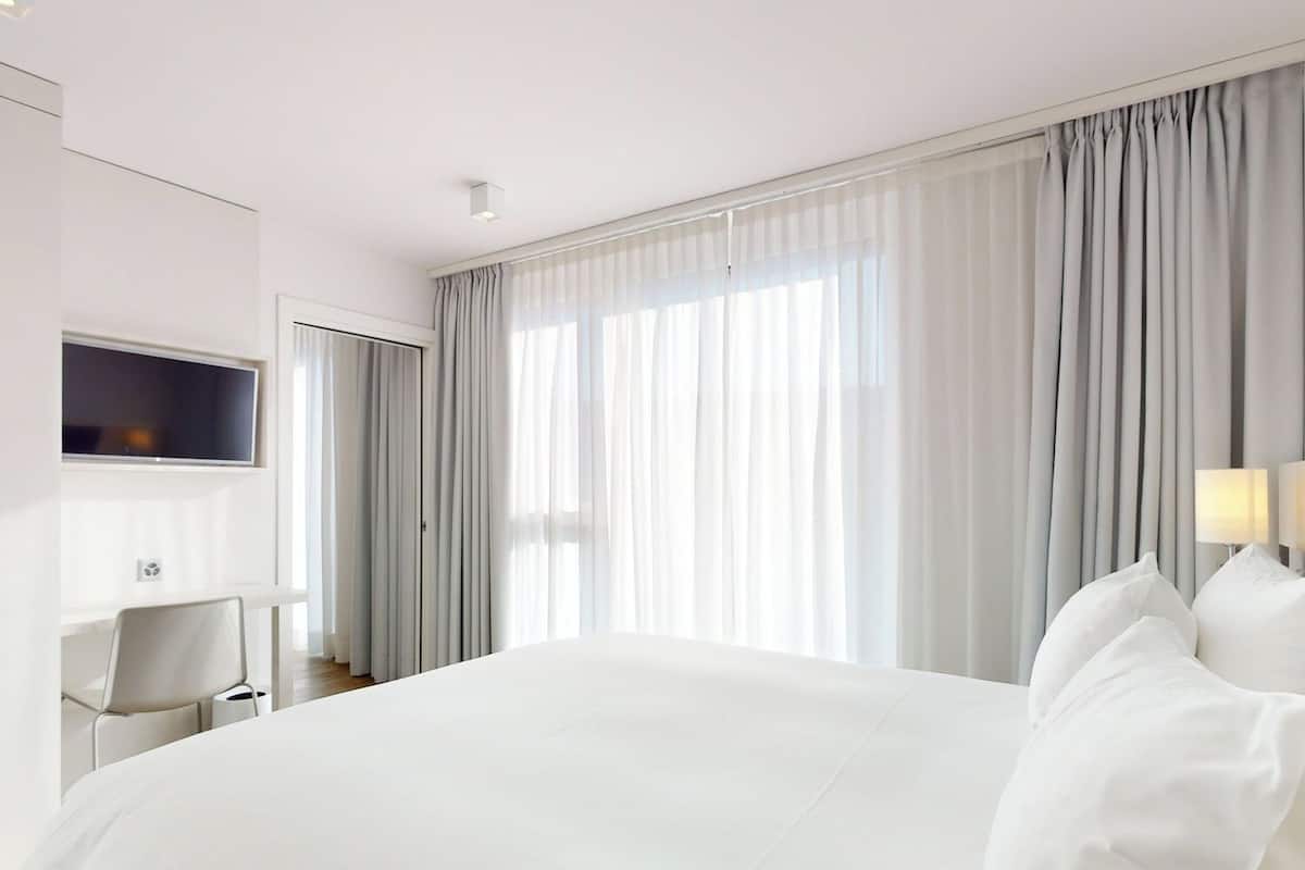 A hotel room with a large bed, a TV mounted on the wall, and a desk with a chair.