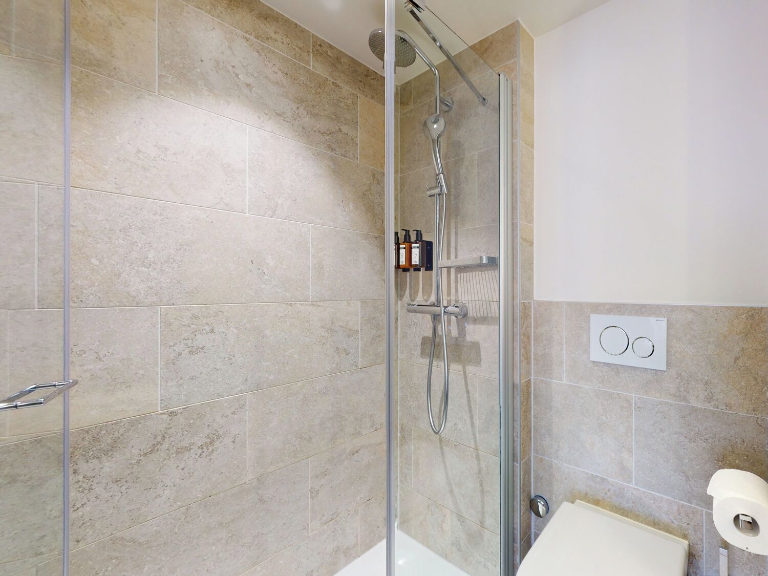 A shower area with a glass door, a handheld showerhead, and a wall-mounted control panel.