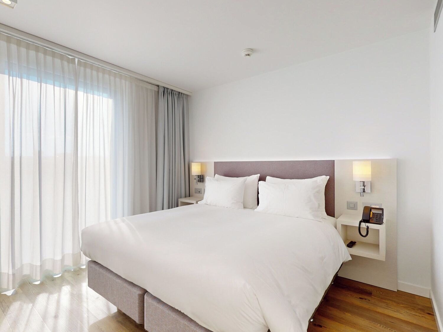 Une chambre d’hôtel moderne avec un grand lit, une table de chevet avec un téléphone et une fenêtre avec des rideaux.