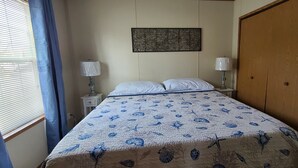 A bedroom with a bed, two bedside tables with lamps, a wooden wardrobe, and a wall art piece.