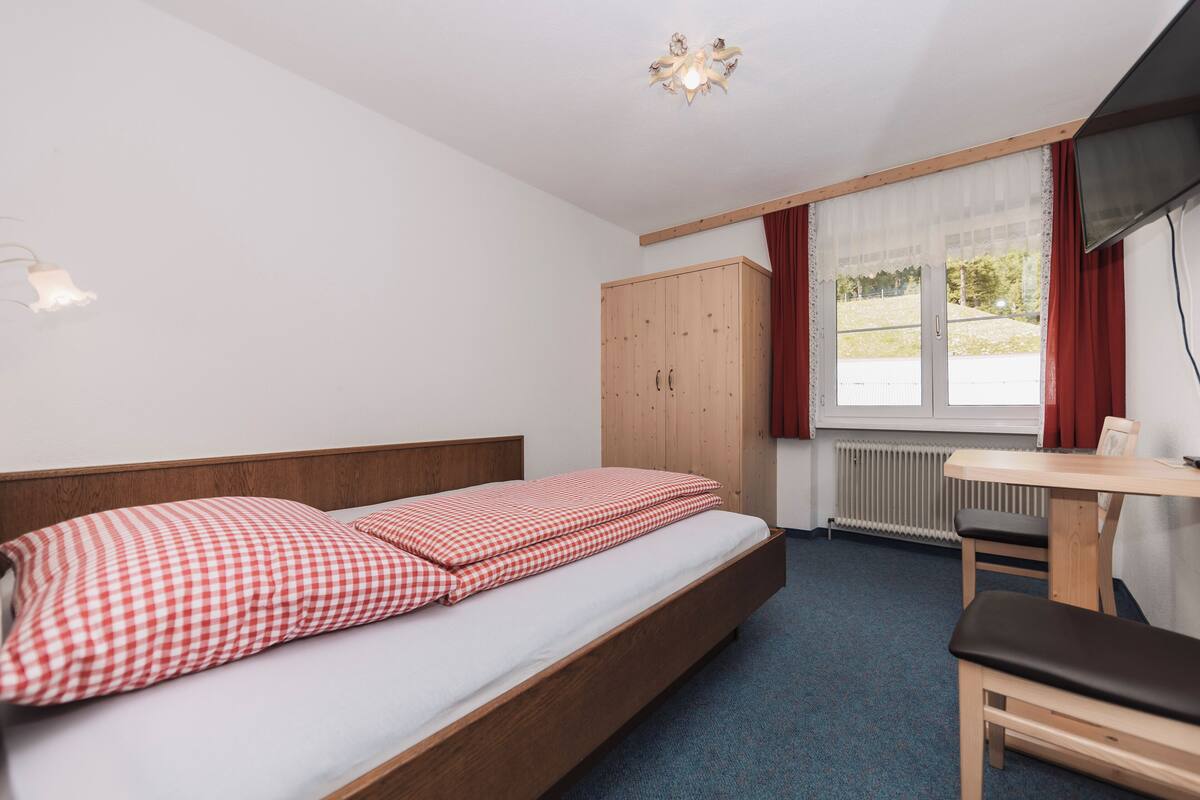 A bedroom with a bed, a desk, and a window.
