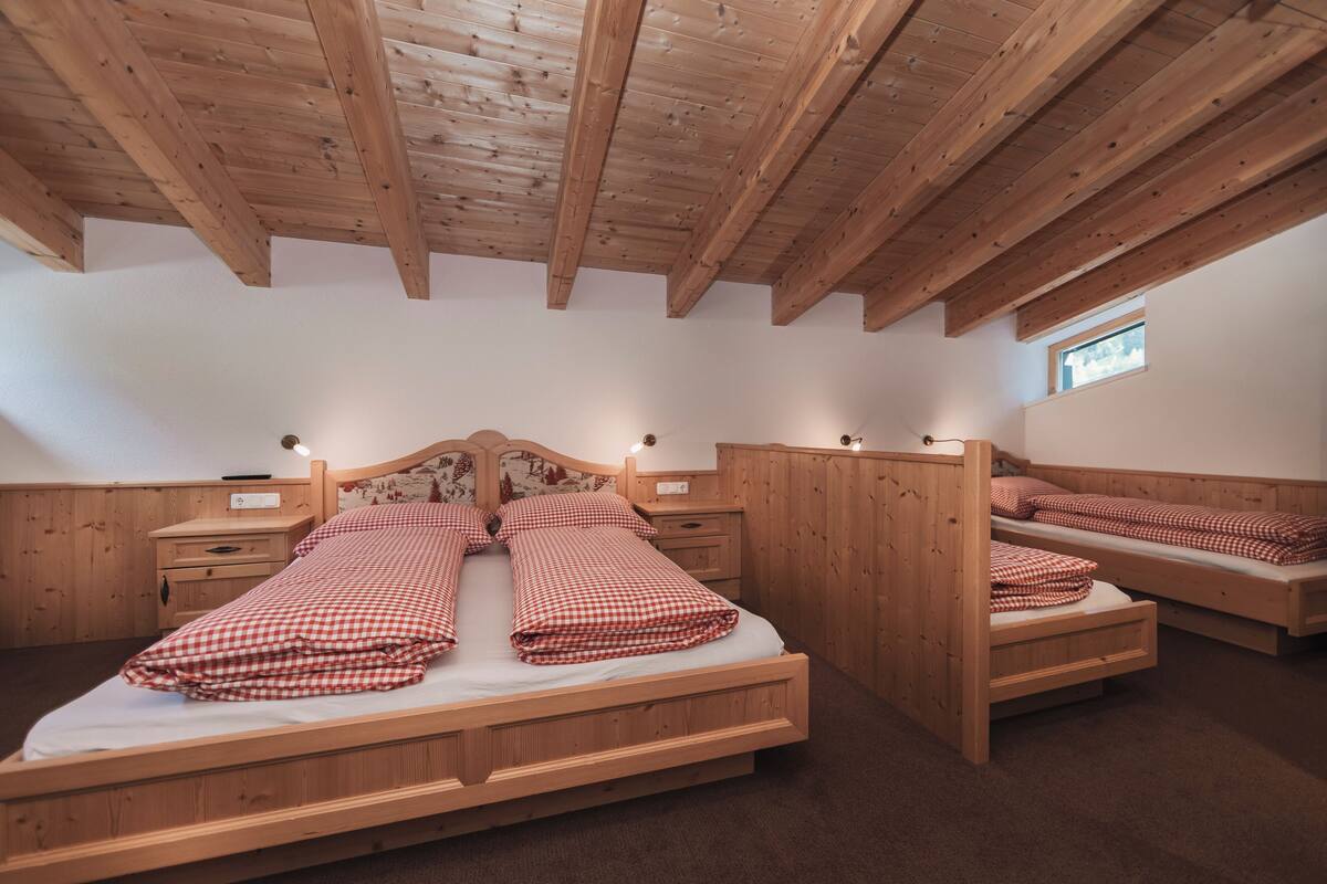 A room with two wooden beds, wooden headboards, and a sloped ceiling.