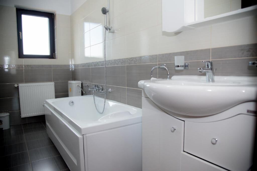 A modern bathroom with a bathtub, a double sink, and a window.