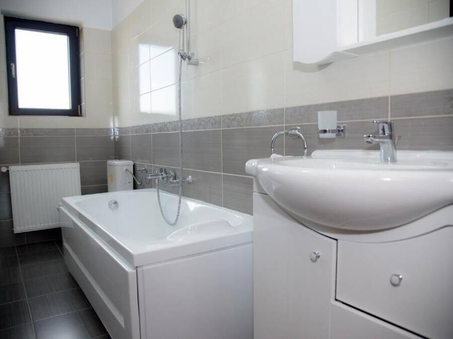 A modern bathroom with a bathtub, a double sink, and a window.