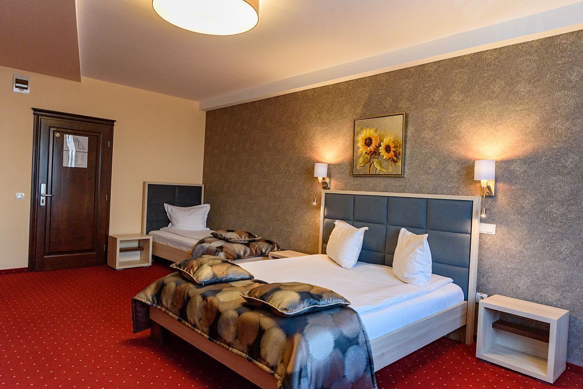 Een hotelkamer met twee bedden, een rood tapijt, een houten deur en een schilderij aan de muur.