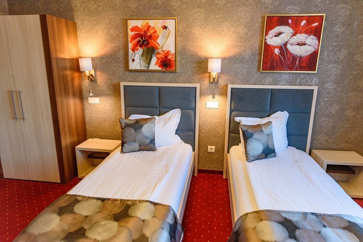 A hotel room with two beds, each with a headboard, bedside tables, and wall-mounted lamps.
