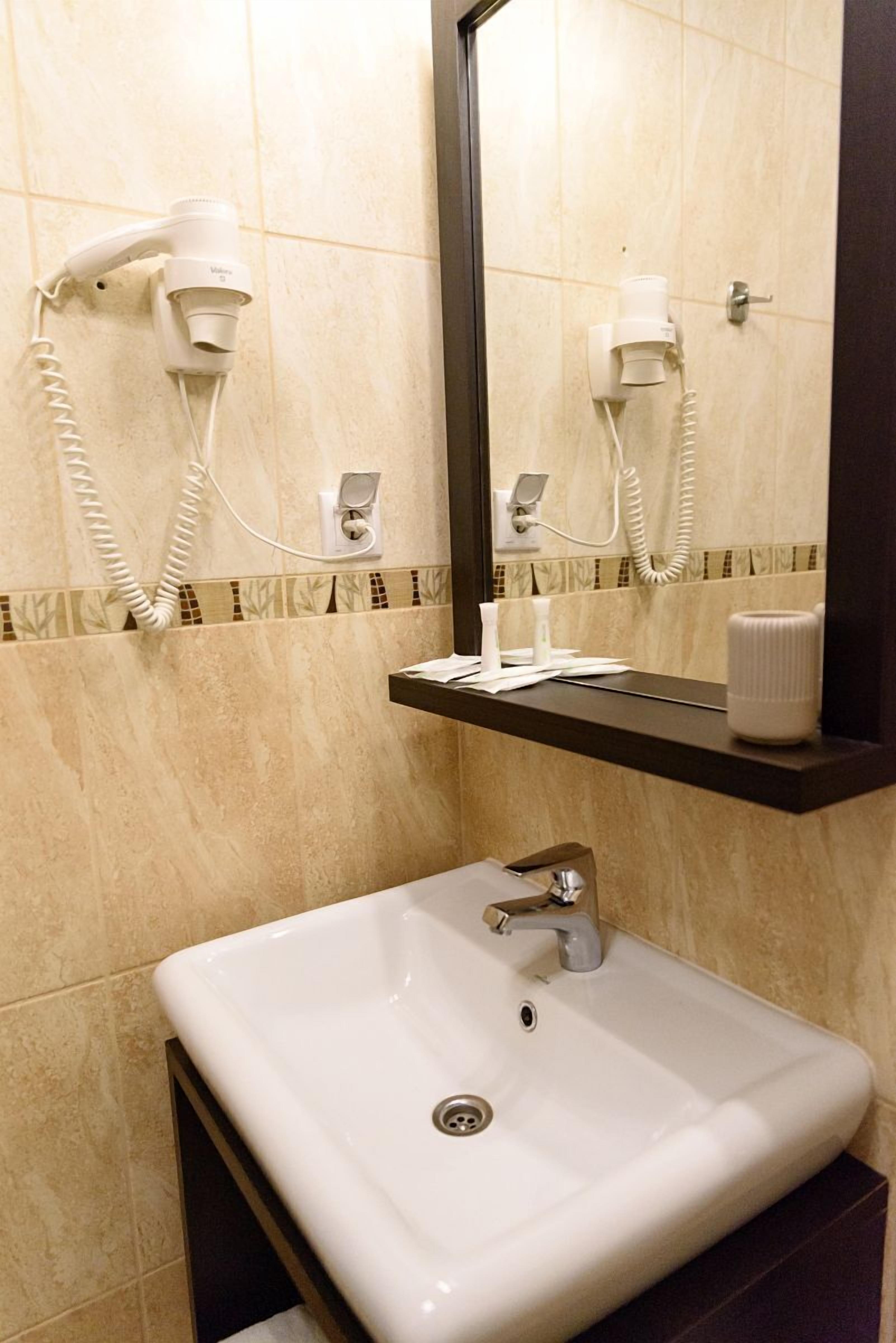 A bathroom with a white sink, a mirror, and two hair dryers mounted on the wall.