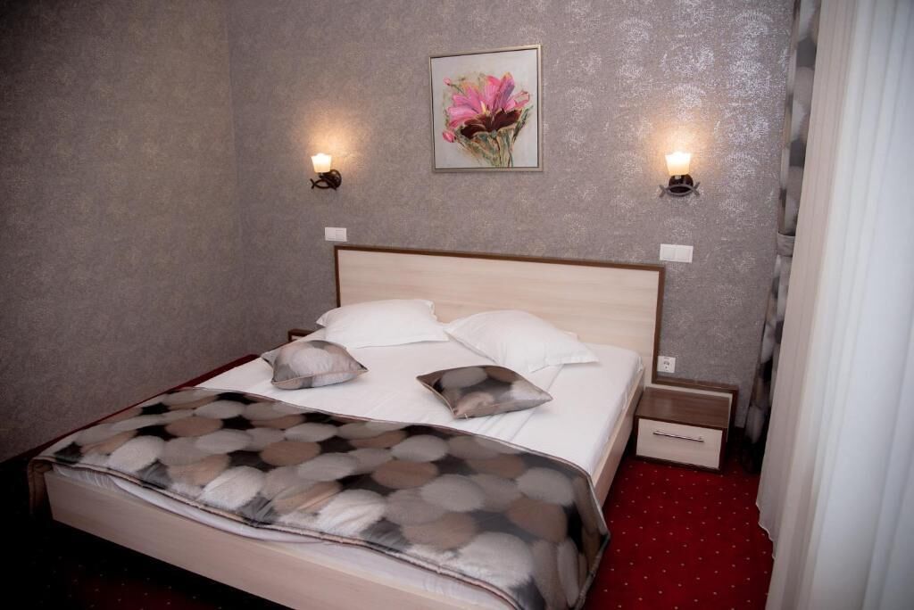 A neatly made bed with a patterned bedspread, two wall-mounted lamps, and a framed floral artwork above the bed.
