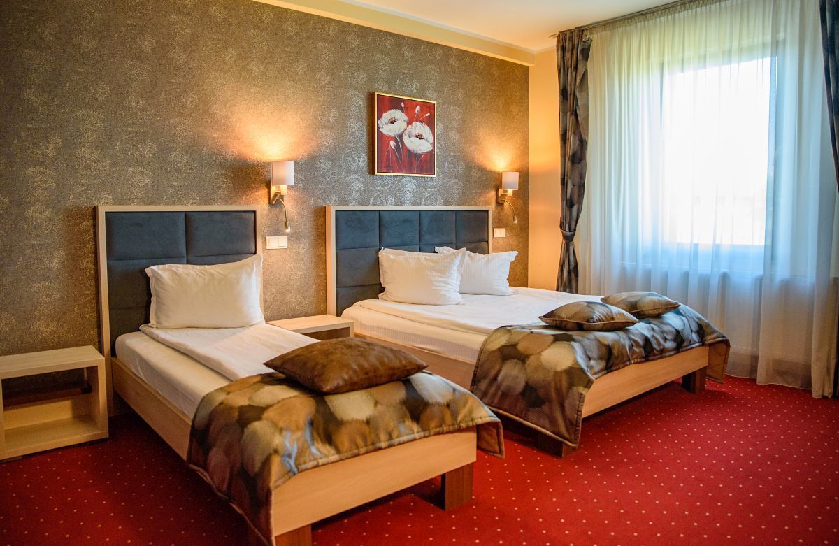 A hotel room with two beds, a red carpet, and a wall with a floral painting.
