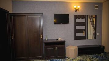 Une chambre dotée d’une grande armoire, d’un téléviseur à écran plat fixé au mur, d’une table de chevet avec une lampe et d’une couvre-lit à motifs.