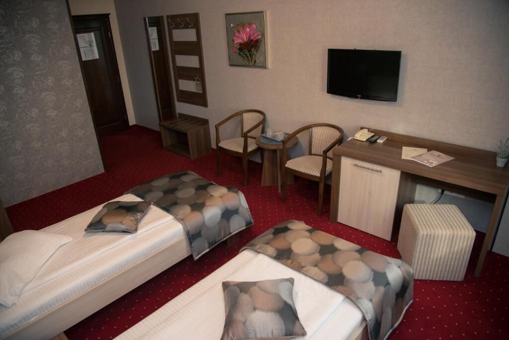 Una habitación de hotel con dos camas, un escritorio, una silla, un televisor y un mueble bajo.