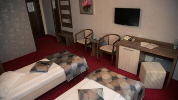 Una habitación de hotel con dos camas, un escritorio, una silla, un televisor y un mueble bajo.