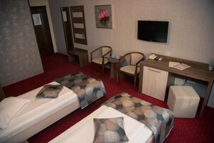 Una habitación de hotel con dos camas, un escritorio, una silla, un televisor y un mueble bajo.