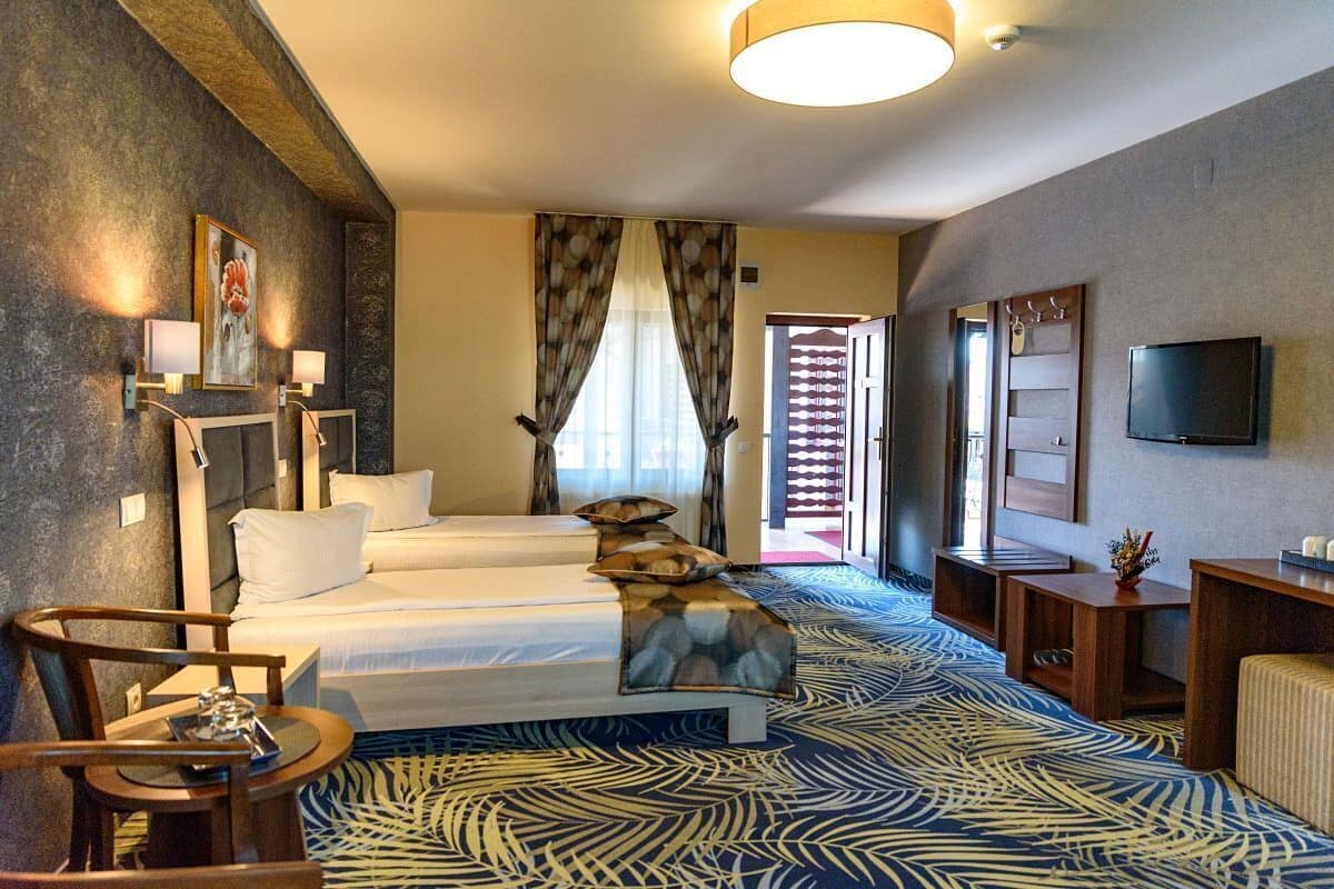 A hotel room with a large bed, two smaller beds, a TV, a desk, and a patterned carpet.
