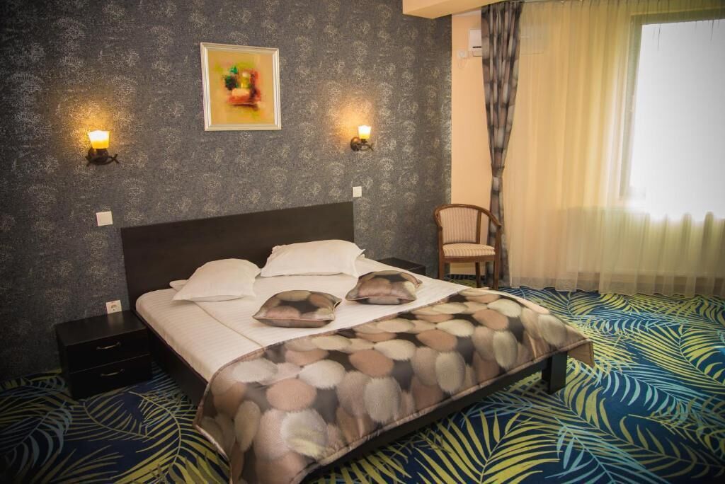A hotel room with a bed, two nightstands, a chair, a painting on the wall, and a window with curtains.