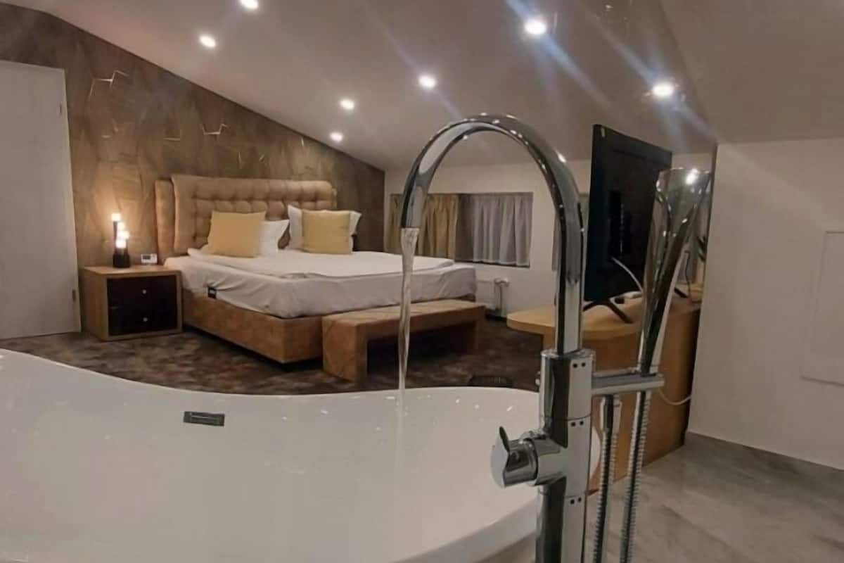 A modern bedroom with a large bathtub, a bed with a headboard, and a nightstand.