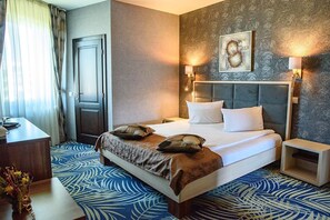 A hotel room with a large bed, two bedside tables, a desk, and a chair. There is a door and a window with curtains. - Hotel Stefani (Sibiu)