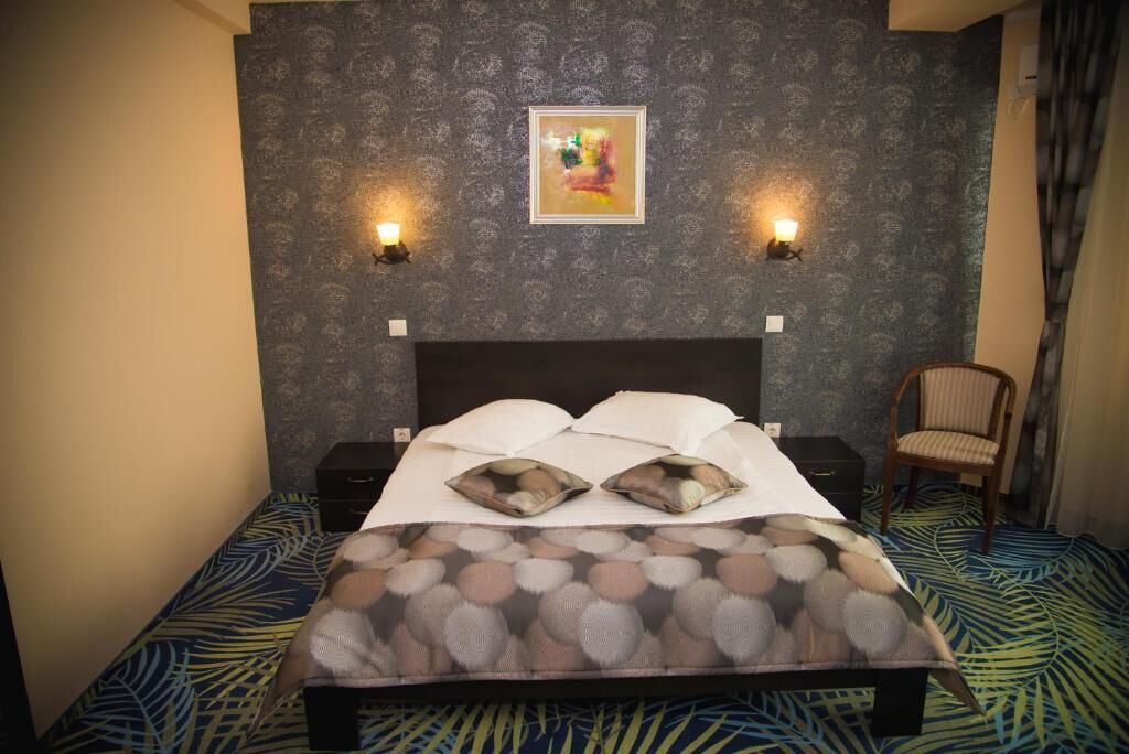 Una cama bien hecha con un edredón estampado, dos lámparas de pared y un cuadro en la pared.