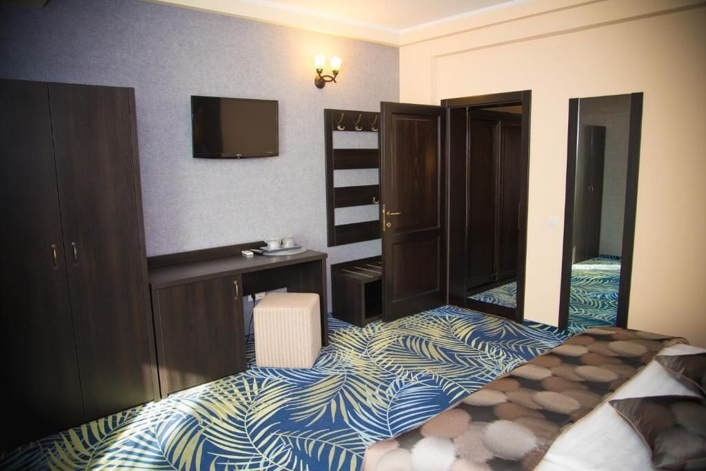 Un dormitorio con cama, cómoda, tocador, espejo y televisor montado en la pared.
