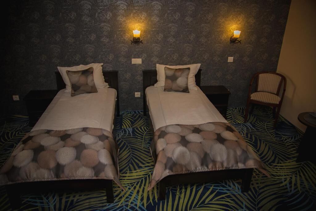 Dos camas individuales con cabeceras, mesitas de noche, lámparas de pared, una alfombra estampada y una silla a rayas.
